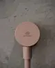 Runder Wandanschlussbogen in Rosé mit Logo von Ideal Standard, montiert auf hellem, strukturiertem Untergrund. Design für Brauseschlauch, offensichtlich funktional und schlicht.